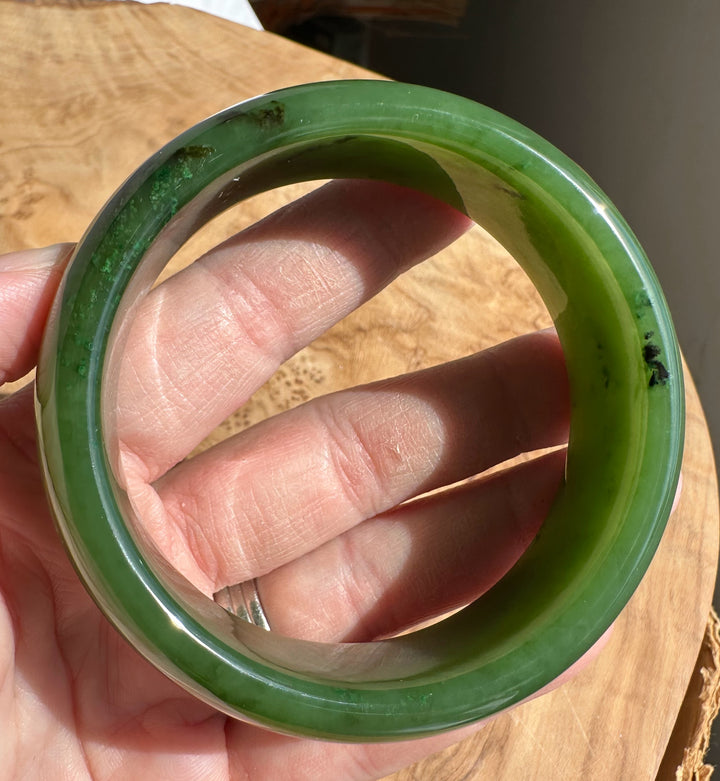 Close-up of a green jade bangle held between fingers, showing a polished surface and natural inclusions.