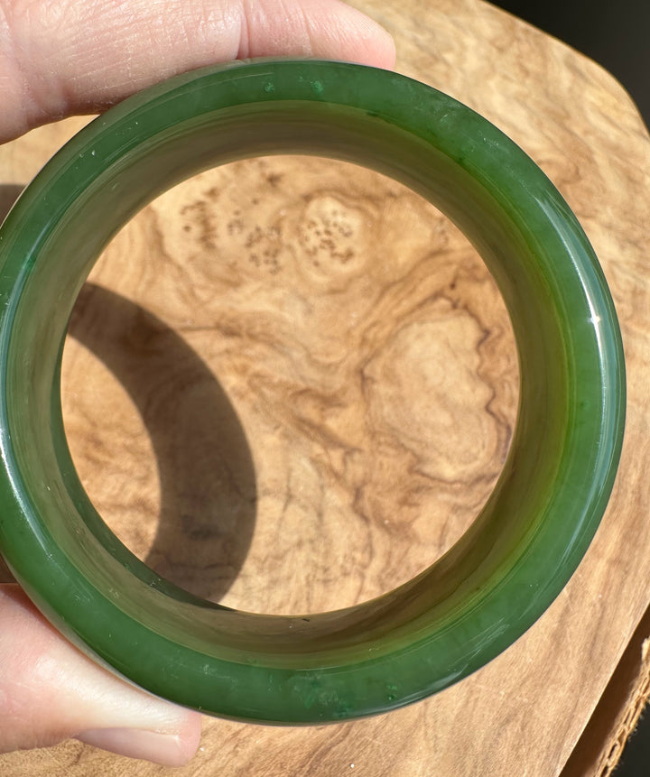 Hand holding a glossy green jade bangle above a wooden surface.