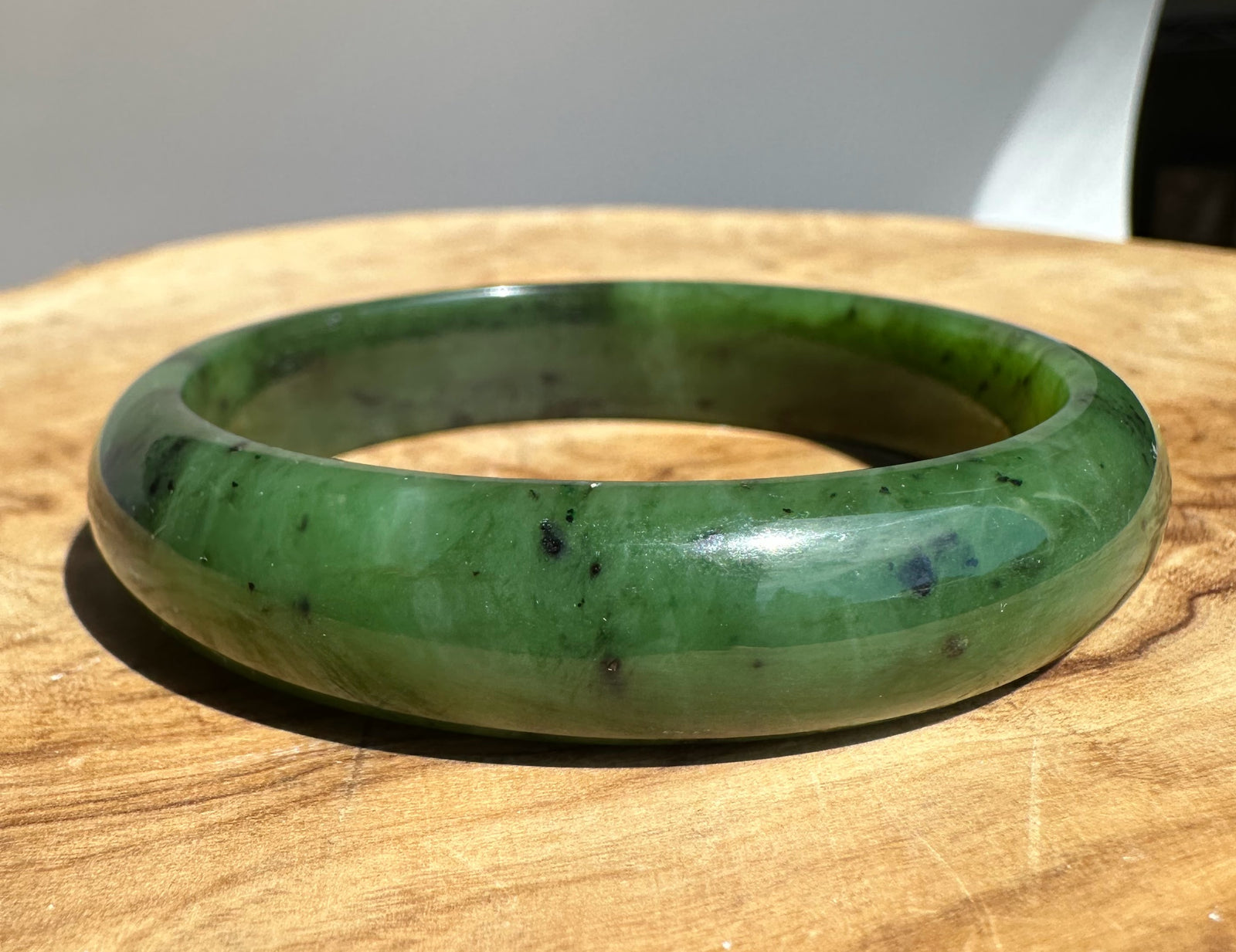 Canadian nephrite jade bangle 58x13 mm with dark specks on a wooden surface