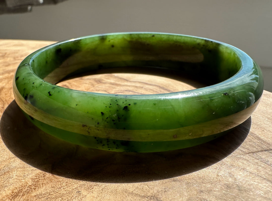 Side view of a green nephrite jade bangle resting on a wooden surface with a neutral background.