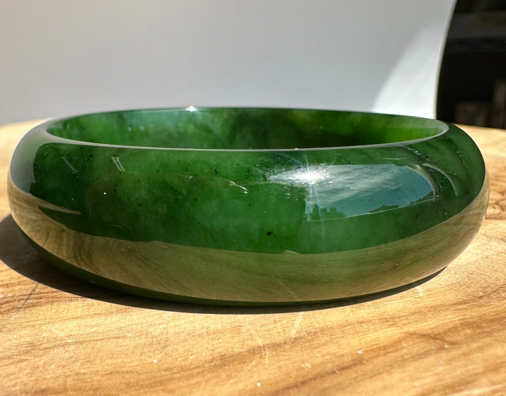 Vivid green jade bangle resting on a wooden surface with a smooth polished edge
