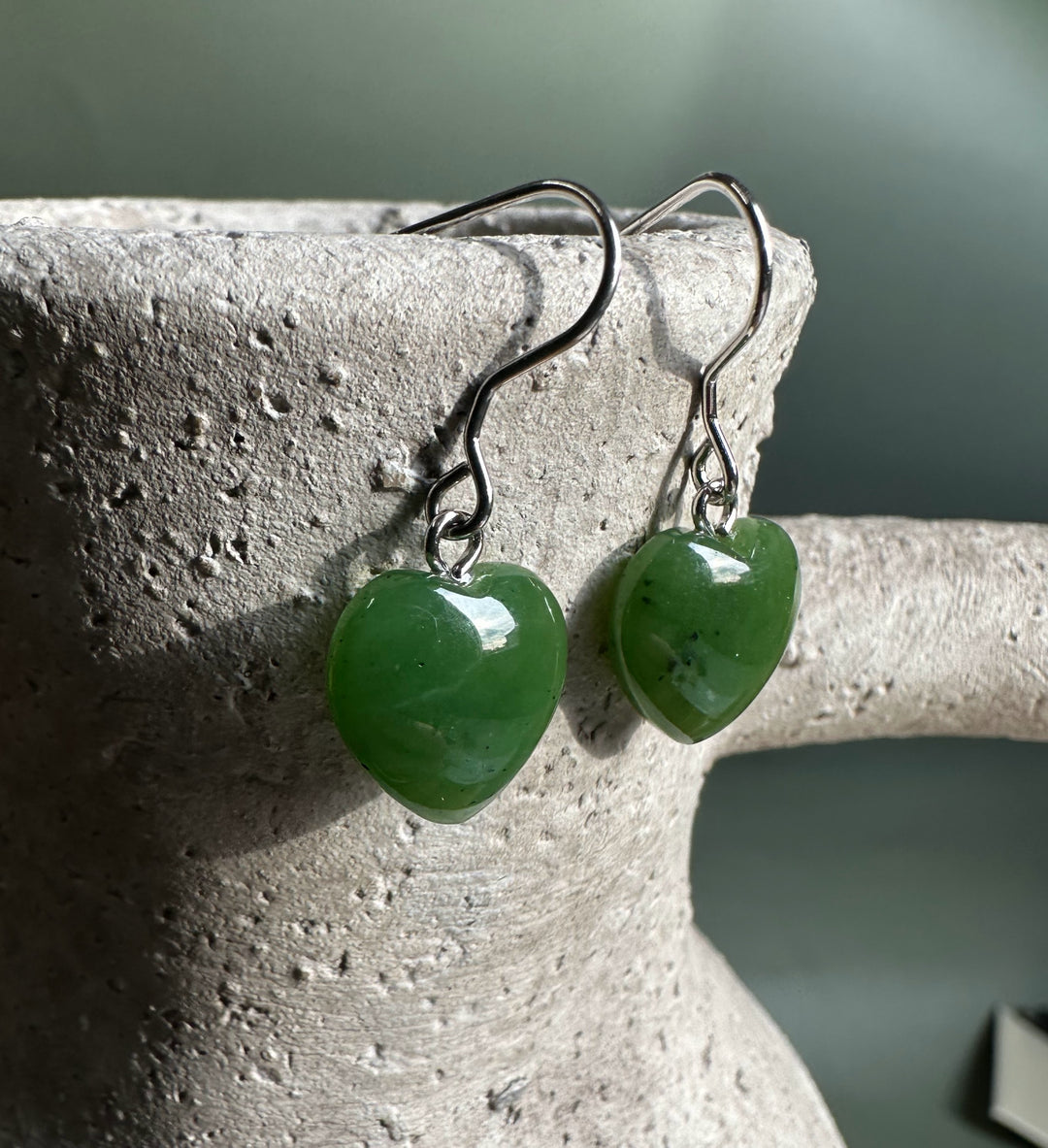 Close up of two green jade heart earrings with silver hooks