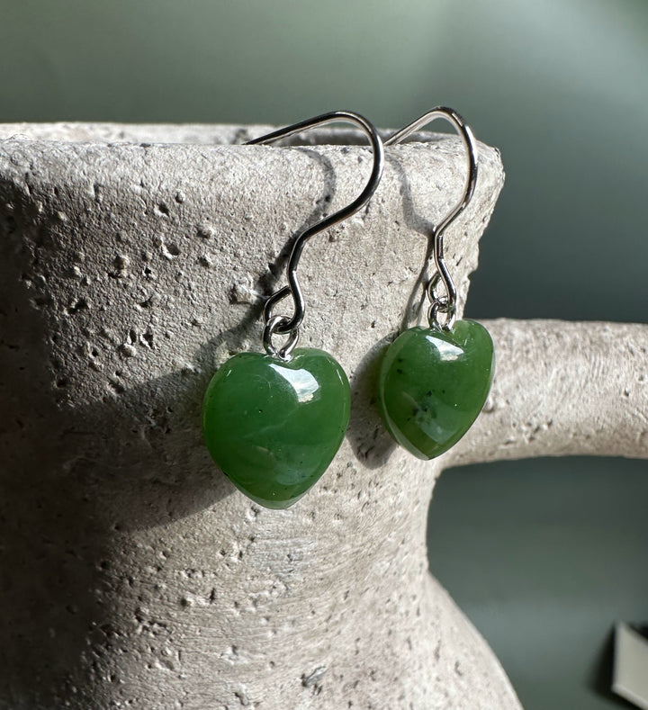 Close up of two green jade heart earrings with silver hooks