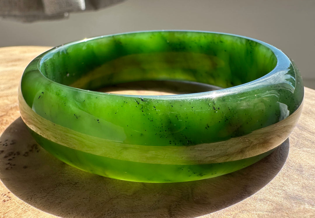 Jade bangle 57 x 17mm in bright green resting on a wooden surface