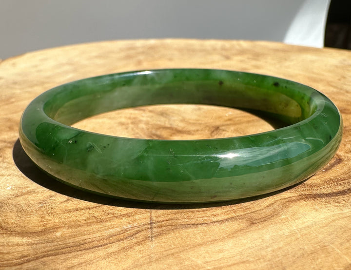 Canadian Jade bangle 60 x 11 mm in a glossy green hue resting on a wooden surface