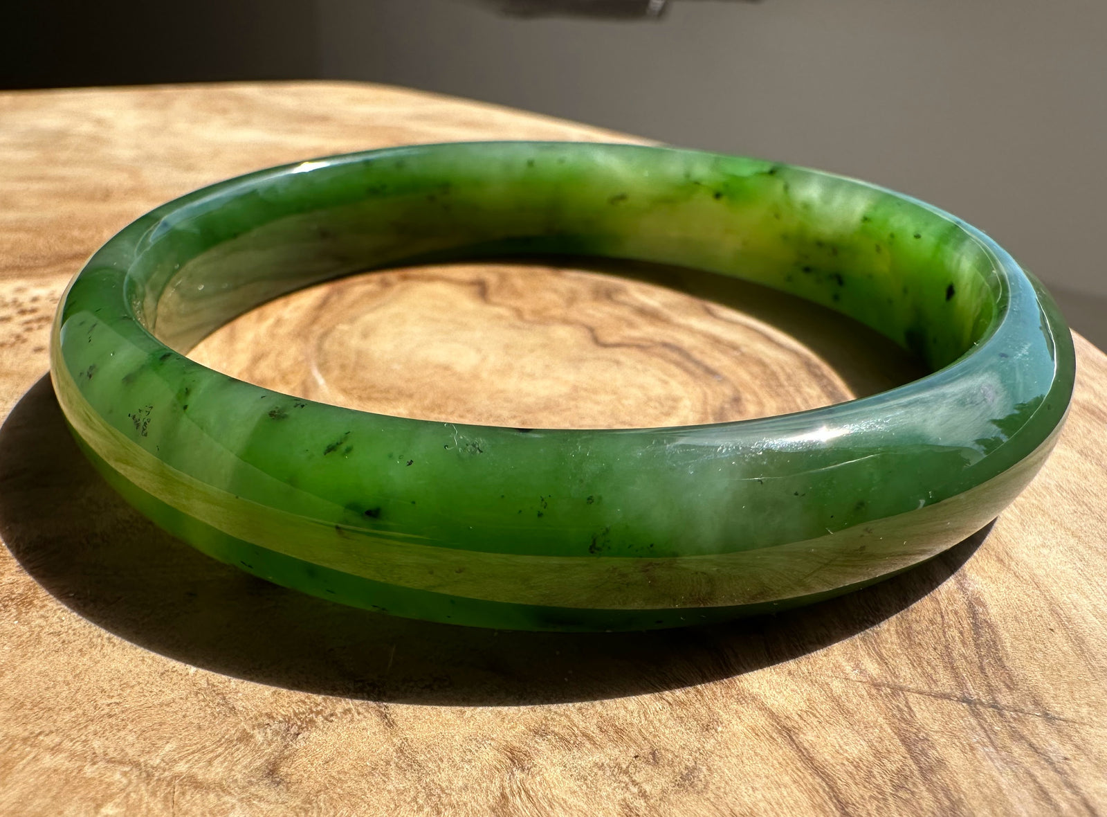 Canadian Jade Bangle 60 x 11mm resting on a wooden surface with a glossy green finish