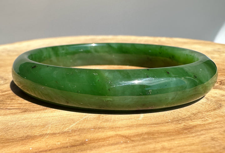 Close up of the green jade bangle showing smooth inner surface and natural color variations on wood.