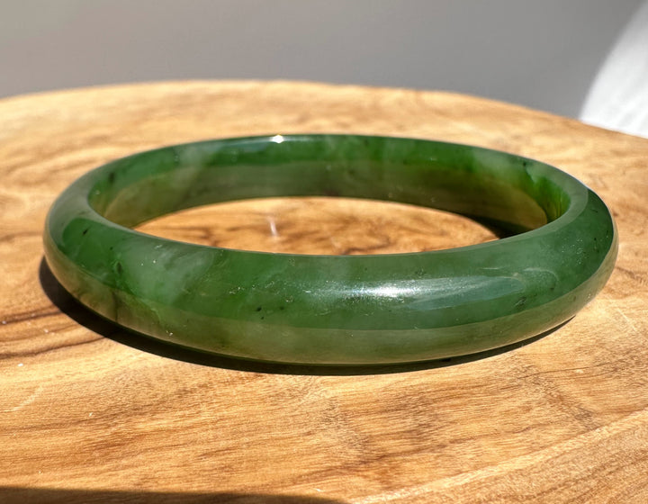 Canadian Jade Bangle 60 x 11mm in rich green rests on a wooden table with a glossy finish.