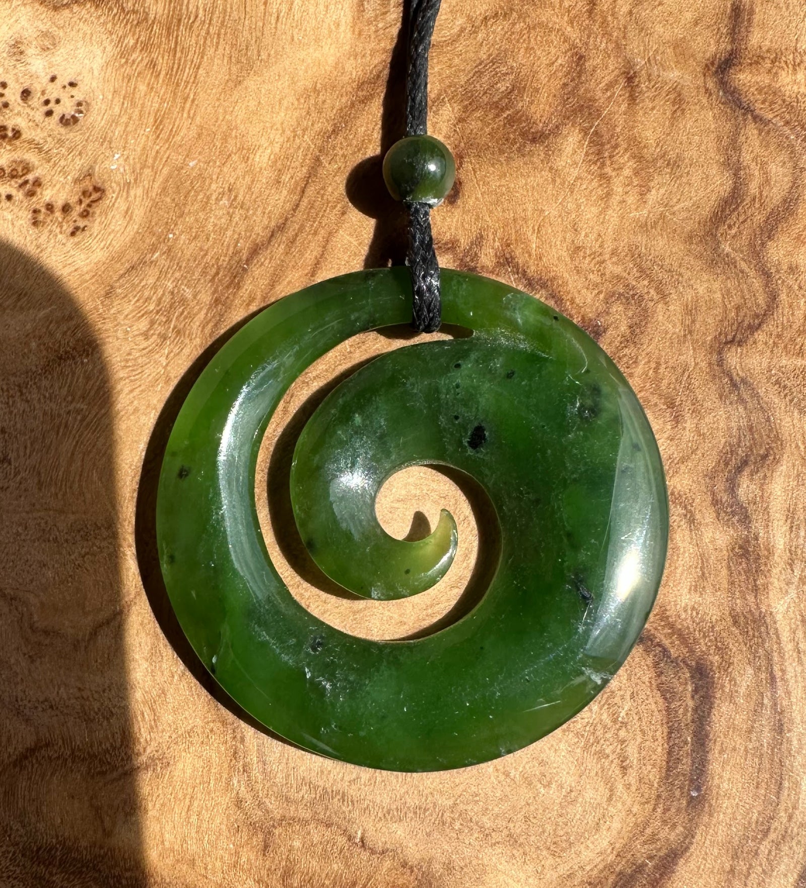 Green jade spiral pendant with a small bead above on a black cord