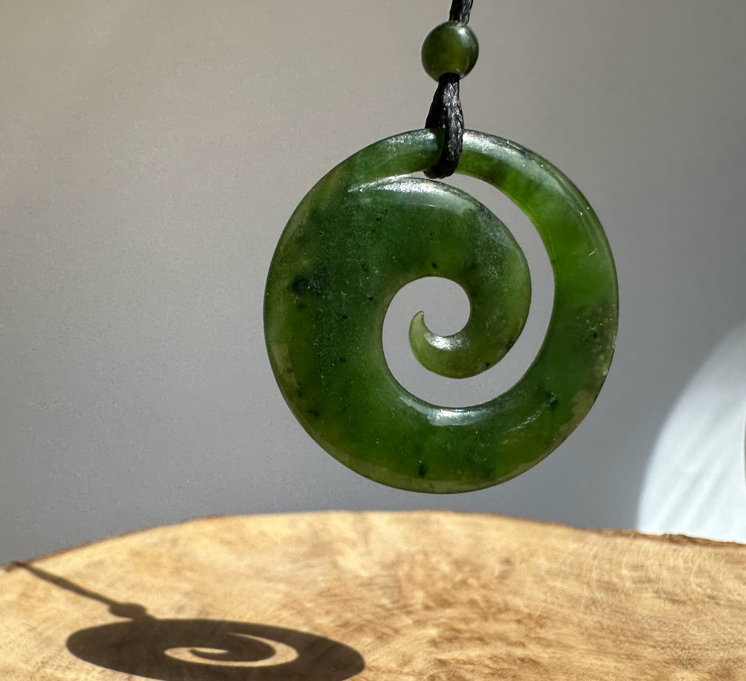 Close up of a green jade spiral pendant with a circular cutout and polished surface on a black cord.