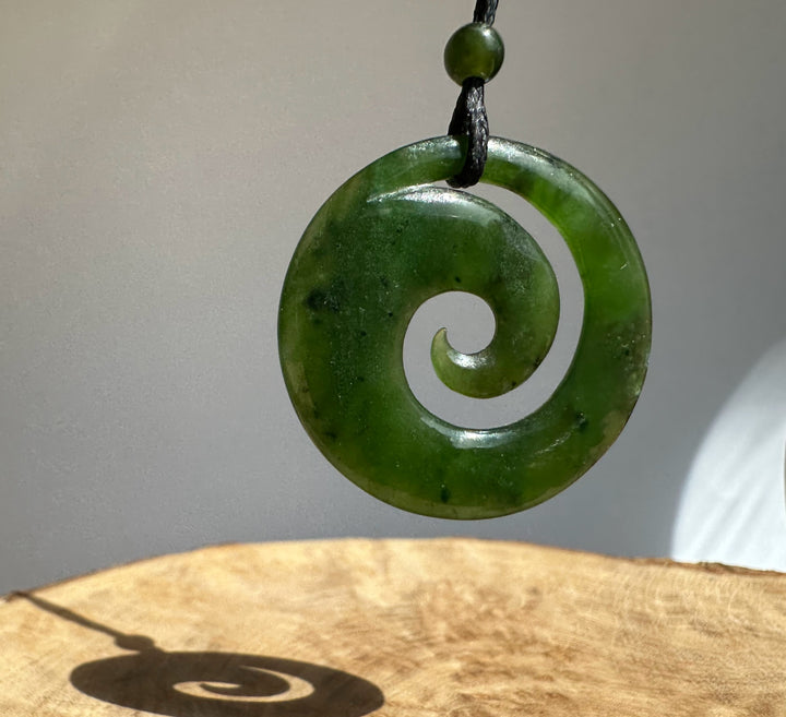 Close up of a green jade spiral pendant with a circular cutout and polished surface on a black cord.