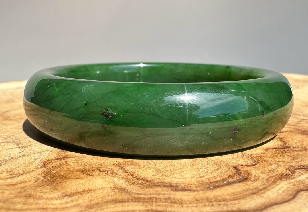 Canadian jade bangle in deep green with a polished finish resting on a wooden surface