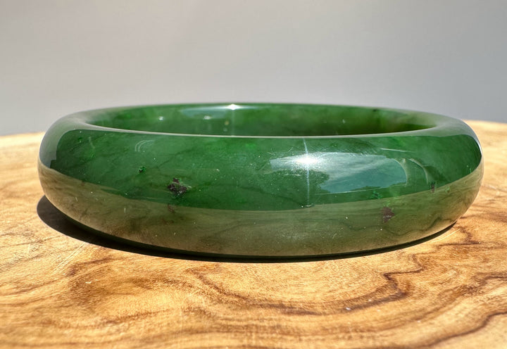 Canadian jade bangle in deep green with a polished finish resting on a wooden surface