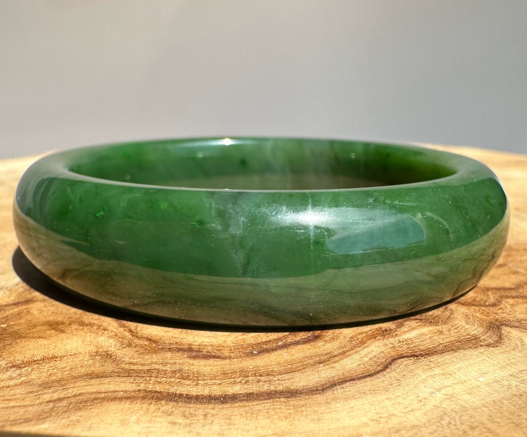 Canadian jade bangle in deep green with light marbling on a wooden surface