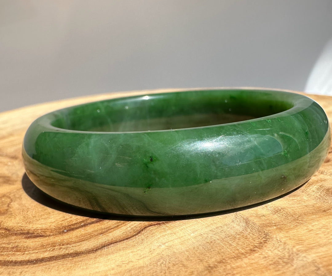 Canadian Jade Bangle 58 x 15.5 mm angled shot highlighting the green jade inner edge on wood surface
