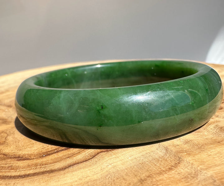 Canadian Jade Bangle 58 x 15.5 mm angled shot highlighting the green jade inner edge on wood surface