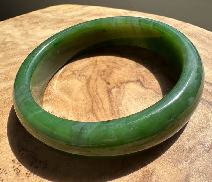 Canadian Jade Bangle 58 x 15.5 mm top edge view with a smooth green glaze resting on wood
