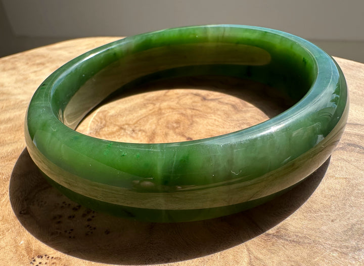 Canadian Jade Bangle 58 x 15.5 mm close up on a wooden surface showing a glossy green circular form
