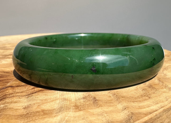 Canadian jade bangle in dark green with small black inclusions on a wooden surface