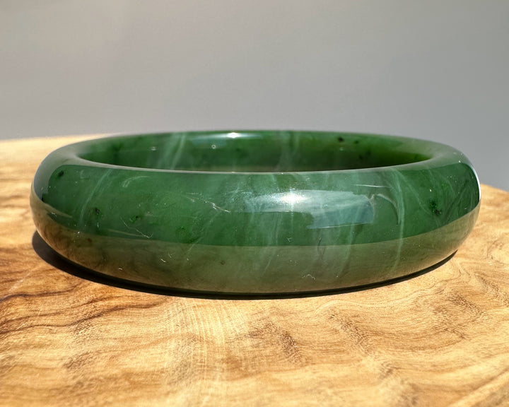 Canadian jade bangle in bright green with subtle dark flecks on a wooden surface