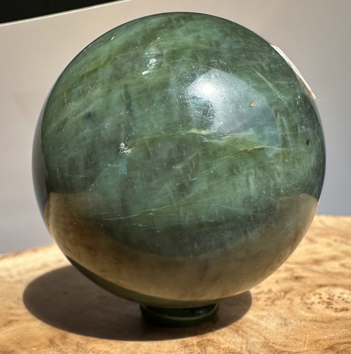 Canadian Jade 66mm sphere viewed from the side with layered greens and a label on the edge
