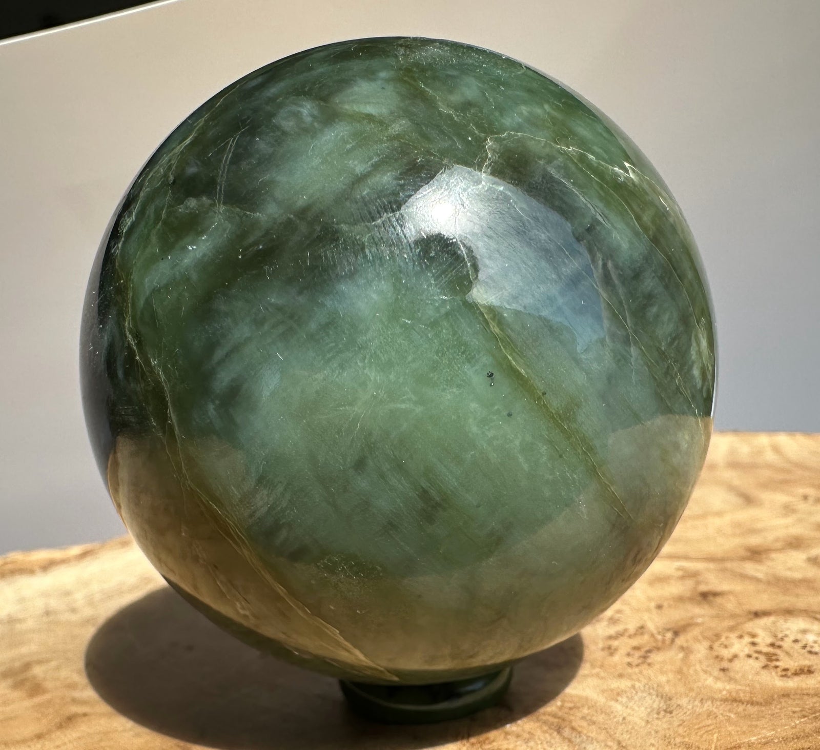 Canadian Jade 66mm sphere close up with dark green color and white veining on a light background