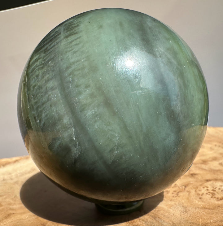 Canadian Jade 66mm Sphere with pale teal hue and subtle marbling, set on a wooden surface.