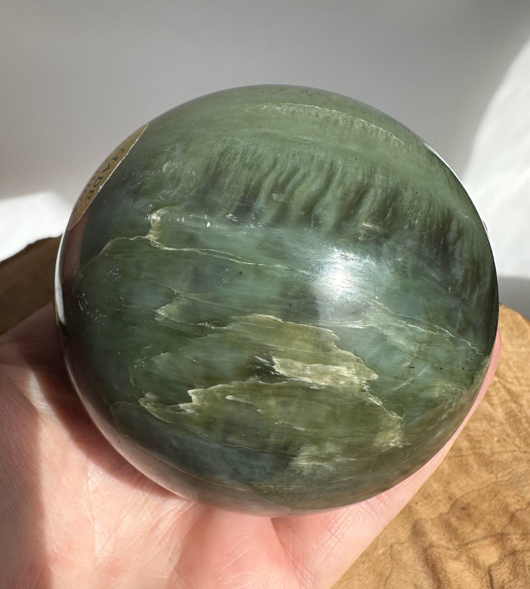 Canadian Jade 66mm sphere held in hand showing green marble like patterns and a smooth surface