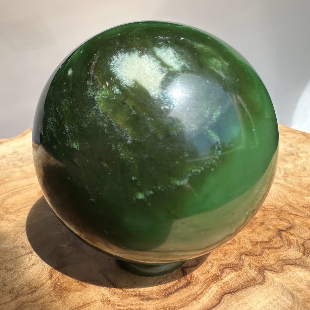 Canadian Jade Sphere 63mm close up of green jade with lighter patches against a pale background.