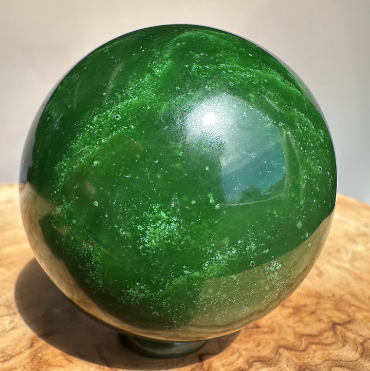 Canadian Jade Sphere 63mm green stone with white flecks on a wooden surface showing a curved top.