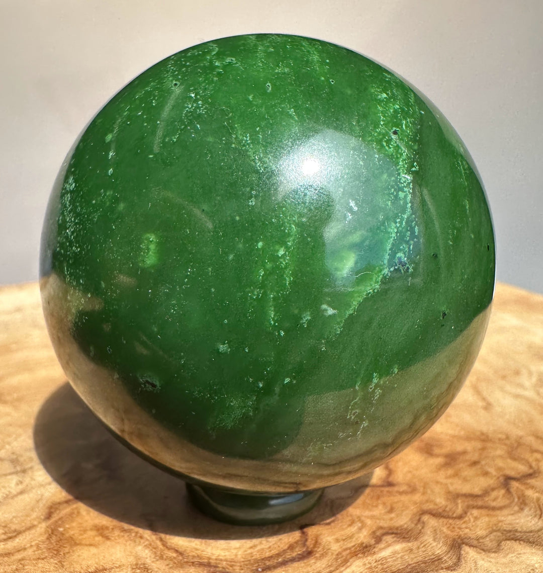 Canadian Jade Sphere 63mm close up showing dark green glossy finish with white flecks on a wooden surface.