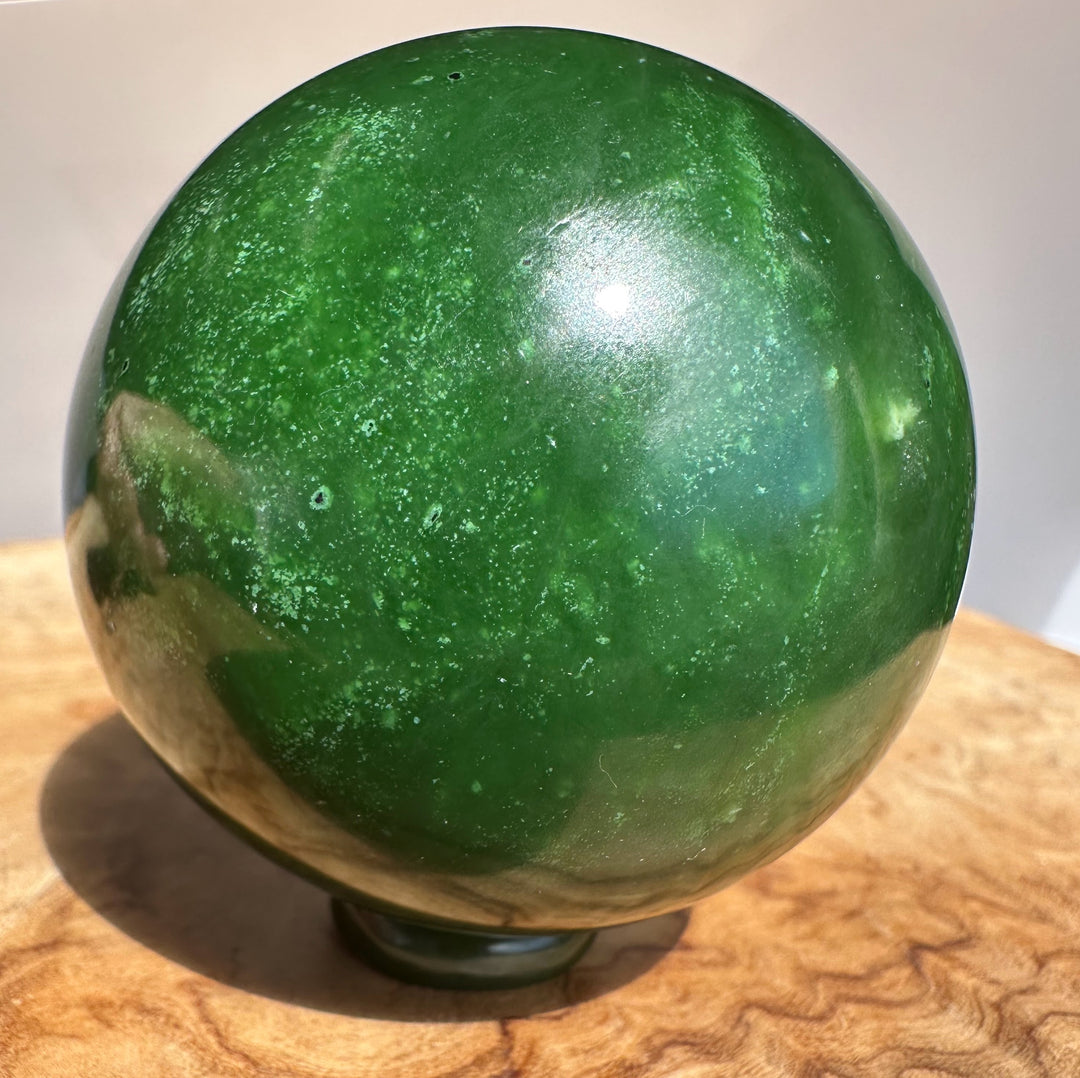 Canadian Jade Sphere 63mm polished green with pale speckles resting on a wooden surface.