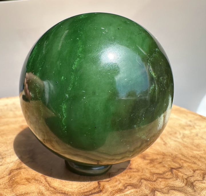 Canadian Jade Sphere 63mm with glossy dark green surface and light streaks, resting on a wooden tabletop.
