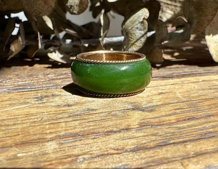 Close-up side view of green jade ring with gold inner band and twisted rope edging on wood