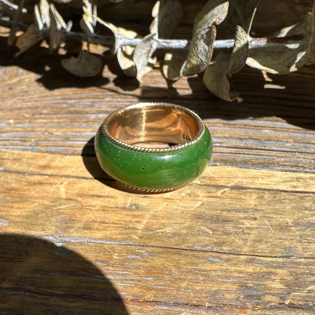 Wide green jade ring with 14k gold inner edge and beaded border on wood.