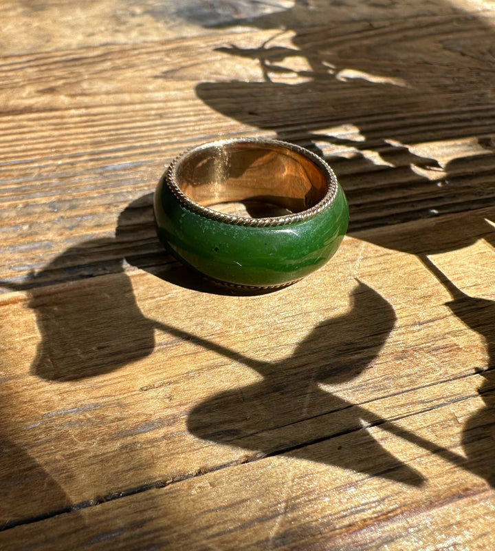 Close-up of a wide green jade ring with gold interior resting on a wooden surface.