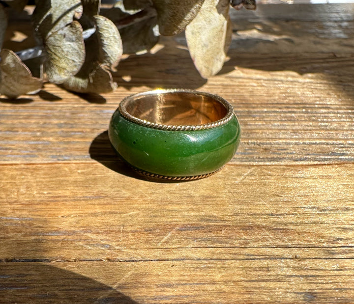 Green jade ring with gold inner band and twisted rope edging resting on a wooden surface