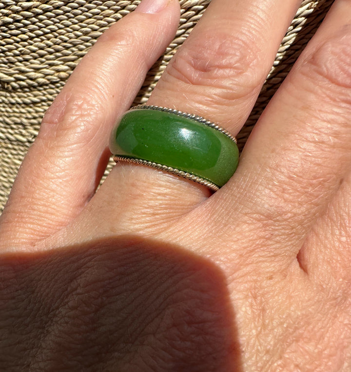 Green jade ring with gold inner band and twisted silver rope edging worn on a finger