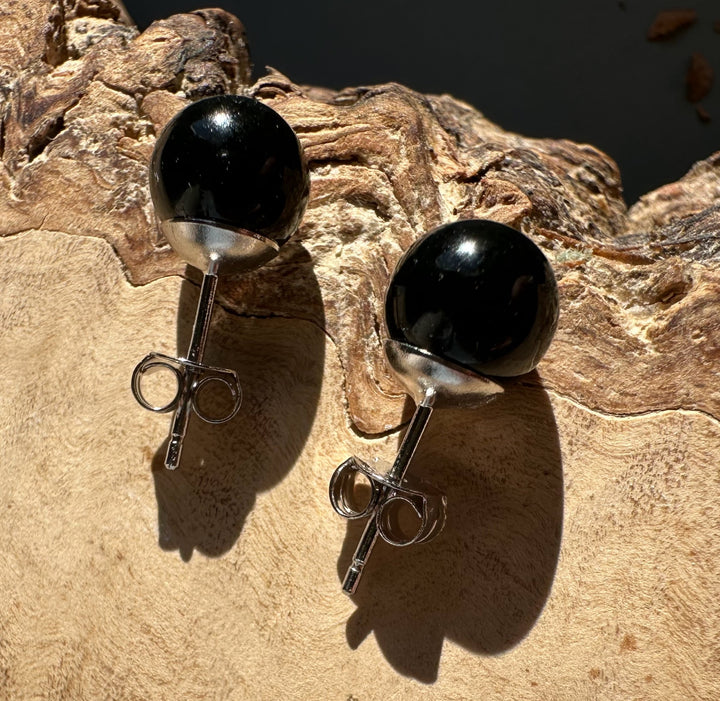 Pair of black jade sphere stud earrings with silver posts on a textured rock surface