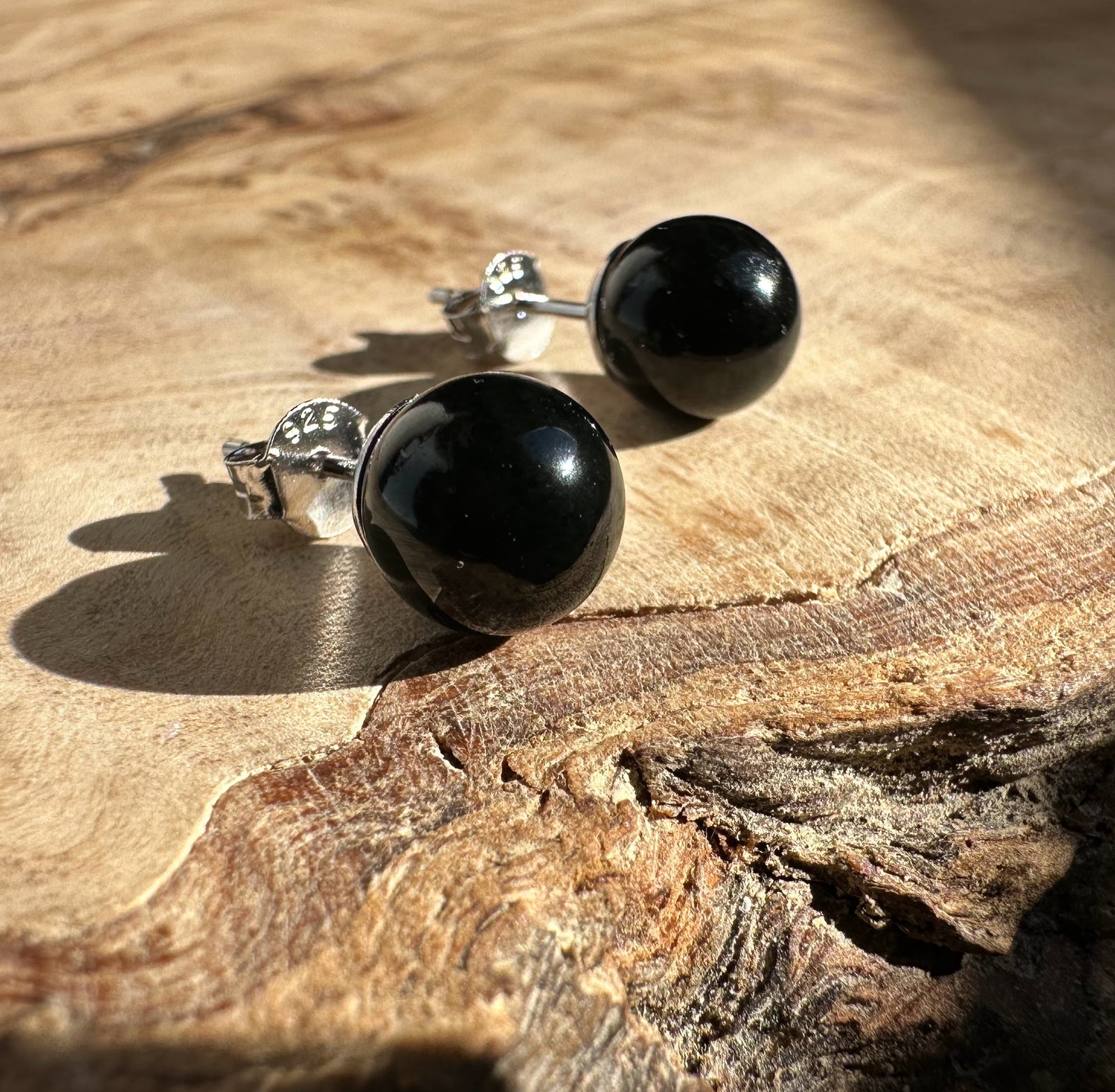Black jade stud earrings with silver posts resting on a wooden surface.