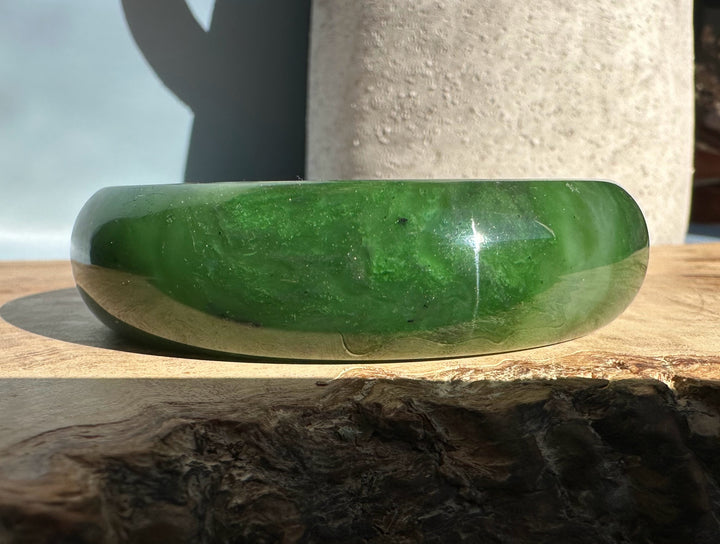 Canadian Jade Bangle 58 x 17.5mm in vivid green shown in side view on a wooden surface