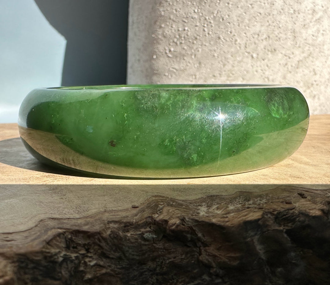 Canadian Jade Bangle in emerald green with a glossy finish resting on a wooden surface
