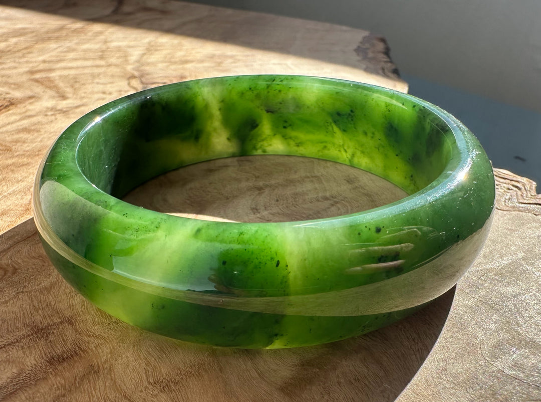 Bright green jade bangle with lime and emerald swirls on a wooden surface