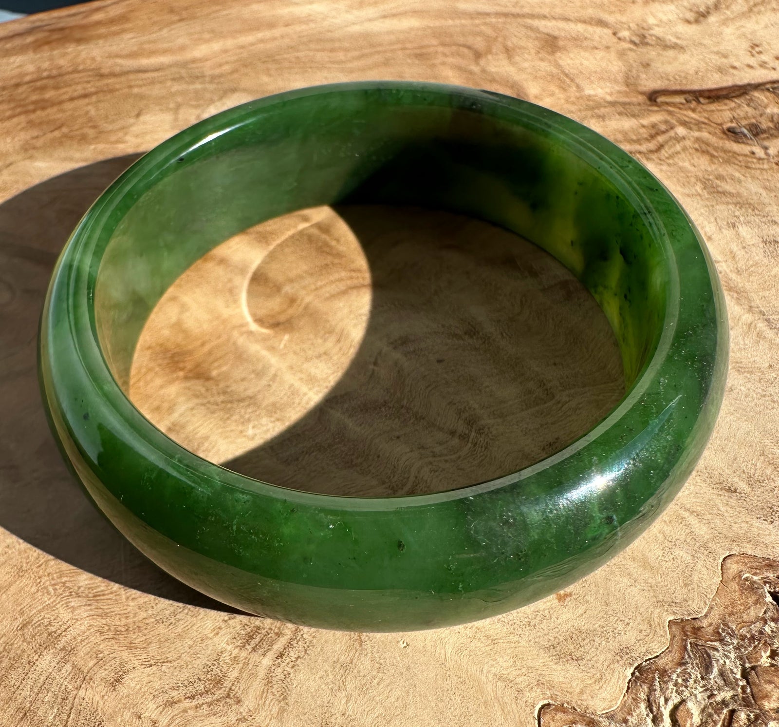 Canadian Jade Bangle 58 x 17.5mm in glossy deep green resting on wood with the circular inner opening visible
