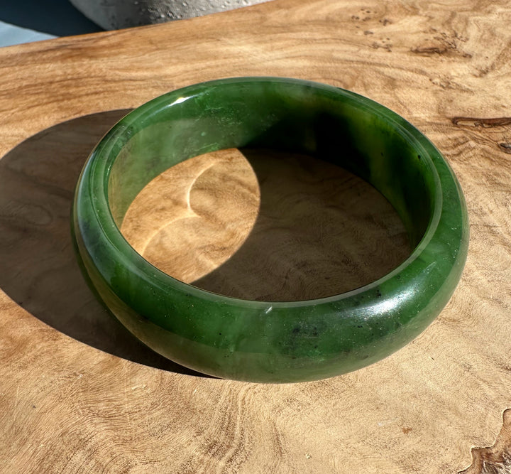 Green jade bangle with varied dark and light green patches on a wooden surface