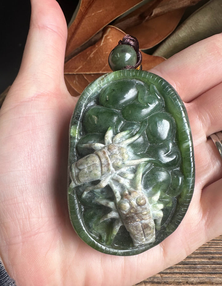 Green jade oval pendant with a detailed spider carving in relief held in a hand