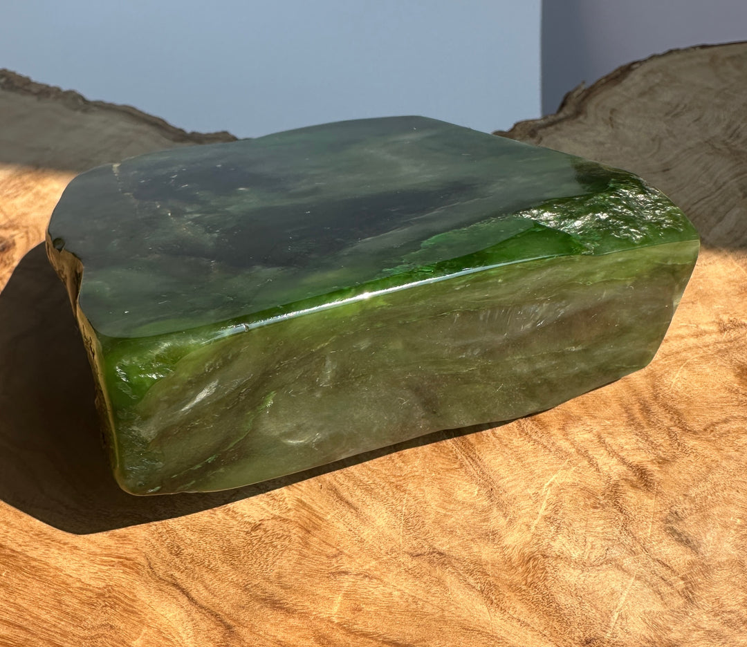 A polished green jade block with natural marbling, displayed on a rustic wood slice surface.