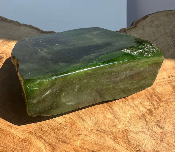 A polished green jade block with natural marbling, displayed on a rustic wood slice surface.