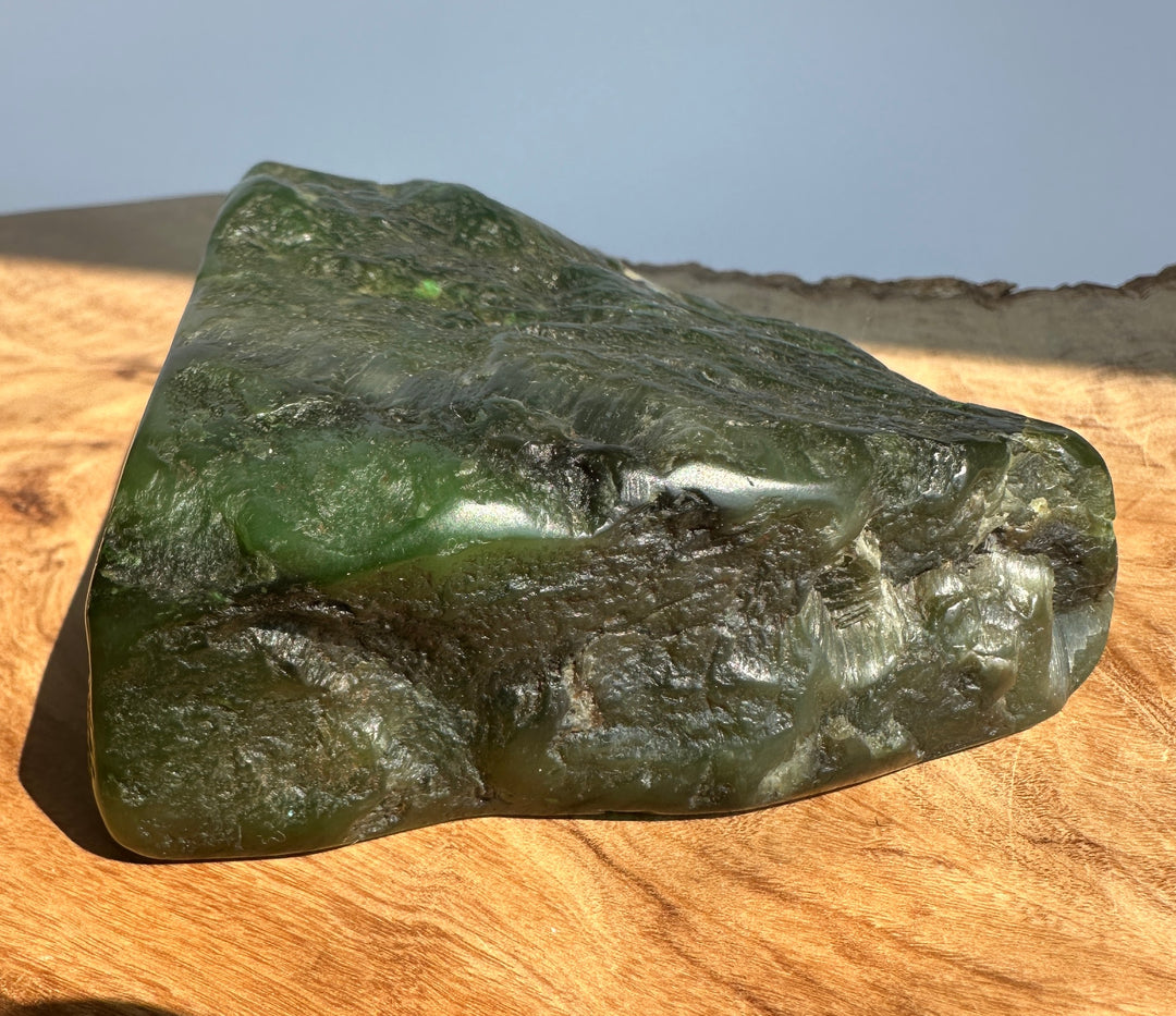 A polished green jade piece with natural marbling, resting on a wooden surface under natural sunlight.