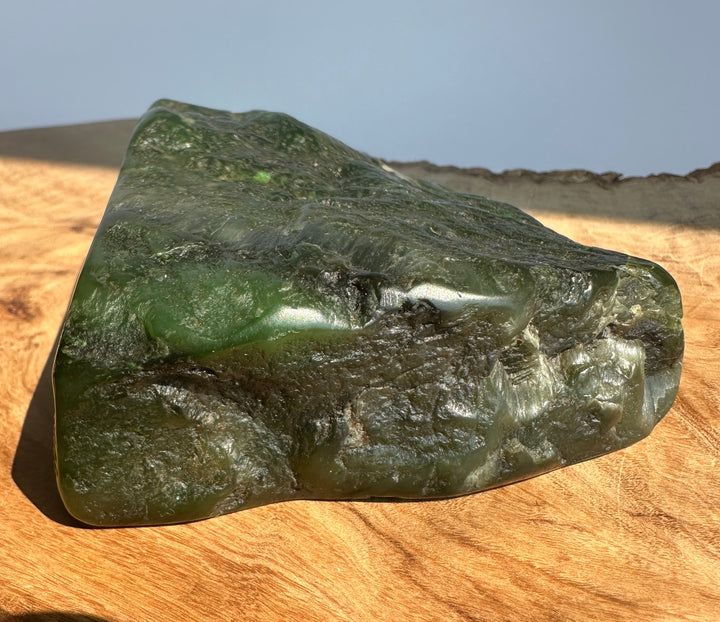 A polished green jade piece with natural marbling, resting on a wooden surface under natural sunlight.
